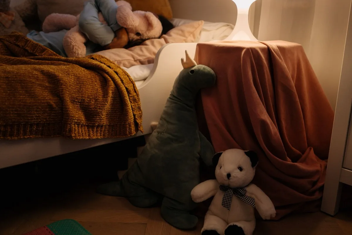 Camera di hotel con lettino aggiuntivo per bambini, giochi morbidi e un piccolo kit di benvenuto su un tavolino